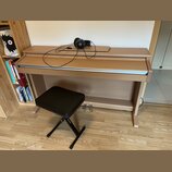 Digitální piano v dřevěněm korpusu s přezeleným povrchem a bílo-černou klaviaturou. Na horní desce nástroje leží černá sluchátka s připojeným kabelem…
