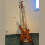 Kytara typu basová s přírodním dřevěným povrchem a hnedým lakem. Na hlavě je viditelné logo "Sadowsky". Nástroj má čtyři struny a je umístěn na černé…