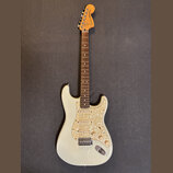 Elektrická kytara s bílým trupem a hmatníkem z tmavého dřeva. Na hlavě je nápis Fender STRATOCASTER. Kytara má tři snímače a plech s perleťovým vzore…