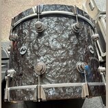 Fotografie zobrazuje buben s šedým, mramorovaným povrchem a chromovaným kováním. Na korpusu jsou umístěna dvě kulatá loga s nápisy „drums“ a „dw“. Po…