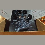 Černý kytarový efekt s texturovaným povrchem a čtyřmi černými ovládacími knoflíky. Na horní straně jsou bílé nápisy OUT, MIDS a TONE, uprostřed modrá…