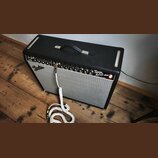Kytarový kombozesilovač s černým texturovaným potahem a stříbrnou textilní maskou. Na předním panelu je vlevo logo Fender a vpravo nápis Twin Reverb-…
