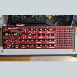Červený semi-modulární syntetizátor s nápisy behringer a NEUTRON. Přední panel obsahuje zahlreichetočítka, přepínače a patchovací pole s označením IN…