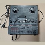 Černý elektronický přístroj s nápisem FOSTEX R8. Horní část obsahuje dvě cívky s logem Fostex a mechanismus pro pásku pod krytem s nápisem Fostex. Sp…