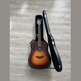 Akustická kytara s tělem typu dreadnought v provedení sunburst (přechod od žluté k tmavě hnědé). Na hlavě nástroje je bílý nápis YAMAHA. Kytara leží…