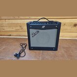 Černý kytarový kombozesilovač s šedou textilní maskou reproduktoru. Na masce je bílý nápis Fender a nad ní se nachází malé kulaté logo. Horní panel o…