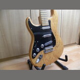 Elektrická kytara s přírodním dřevěným povrchem a černým pickguardem. Nástroj má tři snímače typu single-coil, dva ovládací knofíky a přepínač. Na tě…