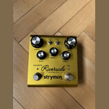 Zlatý kytarový efekt s nápisy Riverside multistage drive a strymon. Na horní straně jsou dva přepínače s označením GAIN (low, high) a PUSH (norm, mid…