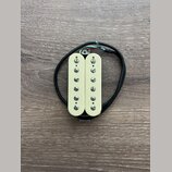 Fotografie znázorňuje humbucker snímač v krémové barvě s dvěma řadami šesti viditelných šroubů. Snímač má připojovací kabel v černém oplastu s odhale…