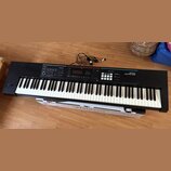 Černý digitální klavír s bílými a černými klávesami. Na pravé straně je bílý nápis Roland JUNO-DS a v sekci ovládání nápisy MODE, KEYBOARD a PHRASE P…