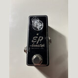 Černý kytarový efekt pedál v kovovém šasi. Na povrchu je bílý nápis „EP -booster BY xotic usa.“ a označení vstupů „IN“ a „OUT“. V horní části je průh…