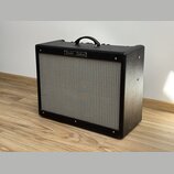 Černý kytarový kombozesilovač s texturovaným povrchem a šedou přední síťovkou. V horní části je umístěn nápis "Fender - Deluxe". Nástroj vykazuje min…