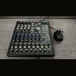 Černý mixážní pult s bílými a barevnými popisky. Na přístroji je viditelné logo PROXTON s označením modelu PRO-10.4+. K mixážní pultu je připojen čer…