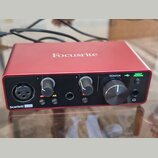 Červené audio rozhraní značky Focusrite. Na předním panelu je nápis Scarlett Solo a ovládací prvky s popisky 1, 2, 48V, AIR, MONITOR a DIRECT MONITOR…