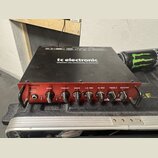 Černý basový zesilovač s červeným předním panelem. Na horní části je bílý nápis tc electronic a text DESIGNED AND ENGINEERED IN DENMARK. Na předním p…