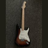 Elektrická kytara s tónem těla v provedení sunburst a světlým hřednicovým dřevě. Na hlavě je viditelné logo Fender. Kytara má bílý pickguard, tři sní…