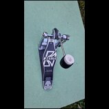 Černý basový pedál s kovovými mechanismy a bílým beaterem. Na stupni je bílé logo TAMA a nápis THE LEGEND IN INNOVATION. Povrch stupně vykazuje známk…