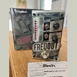 Stříbrný efekt pedál s nápisem FREQOUT a textem NATURAL FEEDBACK CREATOR. Na horní části je logo Digitech, přepínače MOMENTARY a DRY, potenciometr RA…