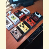 Na černém pedalboardu je umístěno pět efektových pedálů. Zleva doprava jsou vidět pedály s nápisy tc electronic Echobrain ANALOG DELAY (stříbrný), tc…
