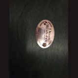 Oválný kovový štítek v měděné barvě připevněný dvěma šrouby. Je na něm uveden nápis Drum Workshop, MADE IN U.S.A. a sériové číslo 003131. Povrch je h…