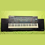 Černý digitální klavír s bílými a černými klávesami. Na ovládacím panelu je vlevo nápis YAMAHA PSR-4500 a vpravo dole na šasi nápis DASSYSTEM. Nástro…