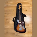Elektrická kytara s trupem v barevnosti sunburst a hnědým hmatníkem, umístěná v černém softcasu. Na hlavě je viditelné logo Fender JAPAN. Kytara má t…