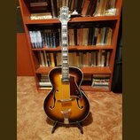 Polodupová elektrická kytara s hnědým sunburst povrchem a f-otvory. Na hlavě je bílý nápis "Parlor". Nástroj má tmavý hmatník, tmavě hnědý pickguard…