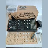 Fotografie zobrazuje analogový syntetizátor Moog Labyrinth v černé barvě s bílými nápisy a ovládacími prvky. Nástroj je doprovázen originálním kartón…