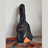 Černý polovrtvný pouzdro na hudební nástroj s oranžovými detaily a lemováním. Na přední straně je bílý nápis CANTO a pod ním menší text MUSIC EQUIPME…