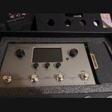 Stříbrný efektový procesor s nápisem AMPERO a podtitulem Amp Modeler & Effects Processor. Zařízení má centrální displej, dva otočné ovladače s popisk…
