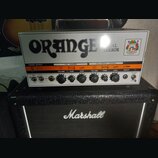 Kytarový zesilovač značky ORANGE s nápisem DUAL TERROR umístěný na kytarovém kombu značky Marshall. Zesilovač má bílý přední panel s ovládacími prvky…