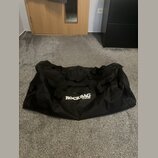 Černá transportní taška z textiledního materiálu s několika úchopy. Na přední straně je bílý nápis ROCKBAG a pod ním menší text by Warwick. Taška vyk…