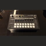 Černá groovebox s bílými popisky a tlačítky. Na horní hraně je nápis Roland vlevo a GROOVEBOX MC-101 vpravo. Zařízení obsahuje několik ovládacích kno…