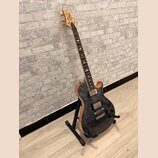 Elektrická kytara s tmavým, pruhovaným povrchem těla a světle hnědými hranami. Na hlavě je viditelné logo značky Cort. Nástroj má dva humbuckery, tři…