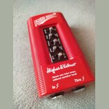 Červený DI box s rýhovaným povrchem. Na horní části je nápis RED BOX a v dolní části logo Hughes & Kettner s varovným textem Never use tube amps with…