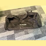Černá transportní taška z textilního materiálu s několika úchopy. Na boku je bílý nápis ROCKBAG a pod ním menší text by Warwick. Taška je otevřená, p…