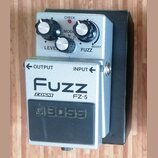 Stříbrný kytarový efekt s černým spínacím pedálem. Na horní části jsou tři ovládací knoflíky a nápisy LEVEL, MODE a FUZZ s možností BOOST. Na přední…