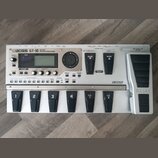 Stříbrný kytarový efektový procesor s nápisem BOSS GT-10 GUITAR EFFECTS PROCESSOR. Zařízení má digitální displej, několik ovládacích tlačítek a v pra…
