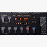 Černý kytarový procesor Boss GT-100 Guitar Amp Effects Processor. Zařízení má digitální displej s nápisem U01-1 a Hi Gain Stack, několik ovládacích k…