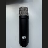 Černý kondenzátorový mikrofon s kovovou stříbrnou mřížkou. Na spodní části těla je bílý nápis RØDE NT1 a pod ním text MADE IN AUSTRALIA P48. Povrch m…