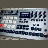 Stříbrný digitální drum machine s názvem Analog Rytm MKII a logem Elektron. Zařízení obsahuje displej, zahlreiche ovládací knofíky, bílé gumové pady…