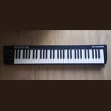 Černá klaviatura s bílými a černými klávesami. Na pravém horním okraji je nápis KEYSTATION 61 MK3 a v pravém dolním rohu logo M-AUDIO. Povrch nástroj…