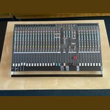 Šedý mixovací pult s velkým množstvím potenciometrů, posuvníků a vstupních konektorů. Na horní části je vidět bílý nápis ALLEN&HEATH a označení model…