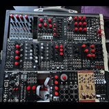Fotografie zachycuje modulární syntetizátor v černém kufru. Na modulech jsou viditelné nápisy TIDES, OAM Time Machine, Timo Rosendahl, QUARKS, WASP 3…