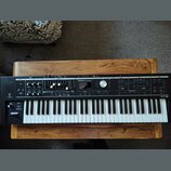 Černý digitální klavír s bílými a černými klávesami, umístěný na dřevěném stole. Na ovládacím panelu je nápis Roland V-Combo VR-09. Přístroj obsahuje…