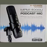 Fotografie znázorňuje krabici s černým kondenzátorovým mikrofonem. Na obalu je uveden název značky marantz PROFESSIONAL a model MPM-4000U PODCAST MIC…