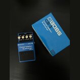 Modrý efekt pedál značky BOSS s nápisem Compression Sustainer CS-3. Na horní části jsou čtyři ovládací knoflíky s popisky LEVEL, TONE, ATTACK a SUSTA…
