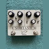 Bílý kytarový efekt s nápisem UNOBTANIUM a logem crazy tube circuits. Zařízení má osm ovládacích knobů s popisky volume, gain, volume, gain, tone, em…