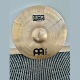 Zlatavý kovový činel s viditelným broušením. Na povrchu jsou nápisy MCS a 20" Medium Ride, v dolní části je logo MEINL. V horní části je malý nečitel…