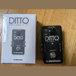 Černý efekt pedál s nápisy DITTO STEREO LOOPER a tc electronic. Na horní části jsou popisky LOOP LEVEL, BACKING TRACK LEVEL a STORE hold to DELETE. V…